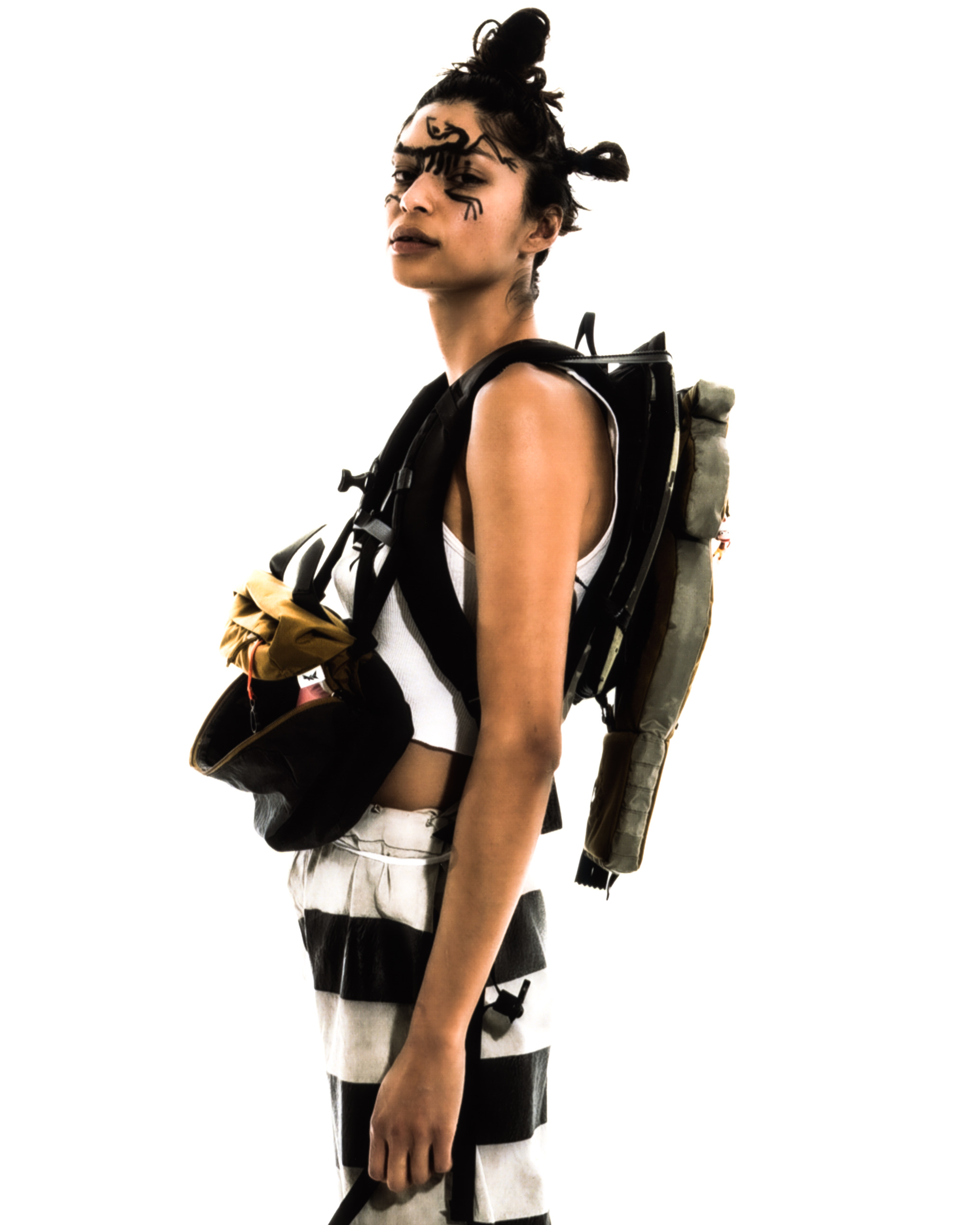 Model towards the camera wearing a structred backpack with striped pants and white tanktop against a white background